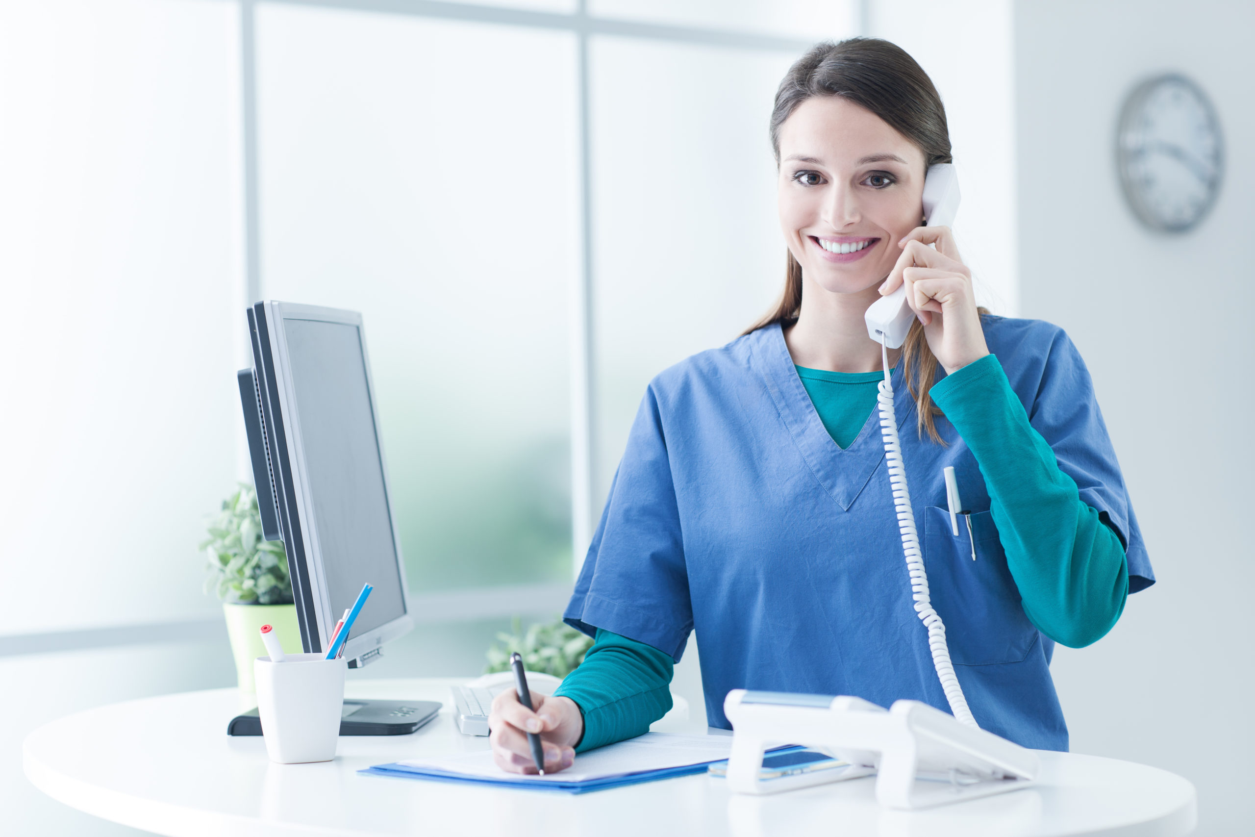 Young female doctor and practitioner working at the reception desk, she is answering phone calls and scheduling appointments